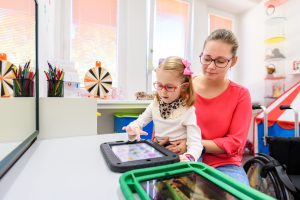 Non-verbal girl living with cerebral palsy, learning to use digital tablet device to communicate. People who have difficulty developing language or using speech use speech-generating devices. By andreaobzerova